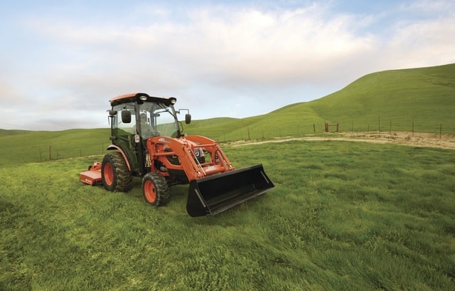 Compact tractor with front loader and brush hog in a field